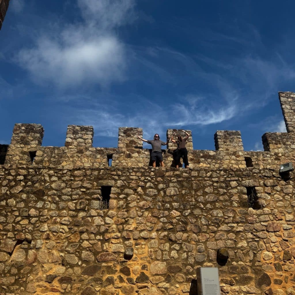 Two readers waving from the top of Almourol Castle’s crenellated walls under a blue sky