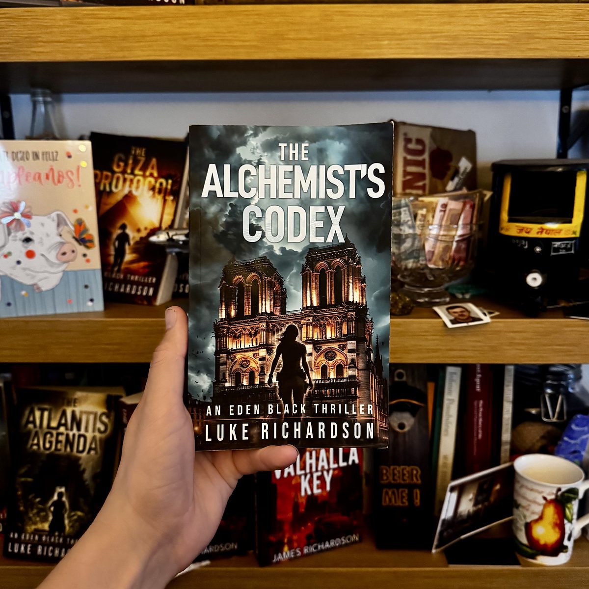 The Alchemist’s Codex held in front of a bookshelf with other Luke Richardson thrillers